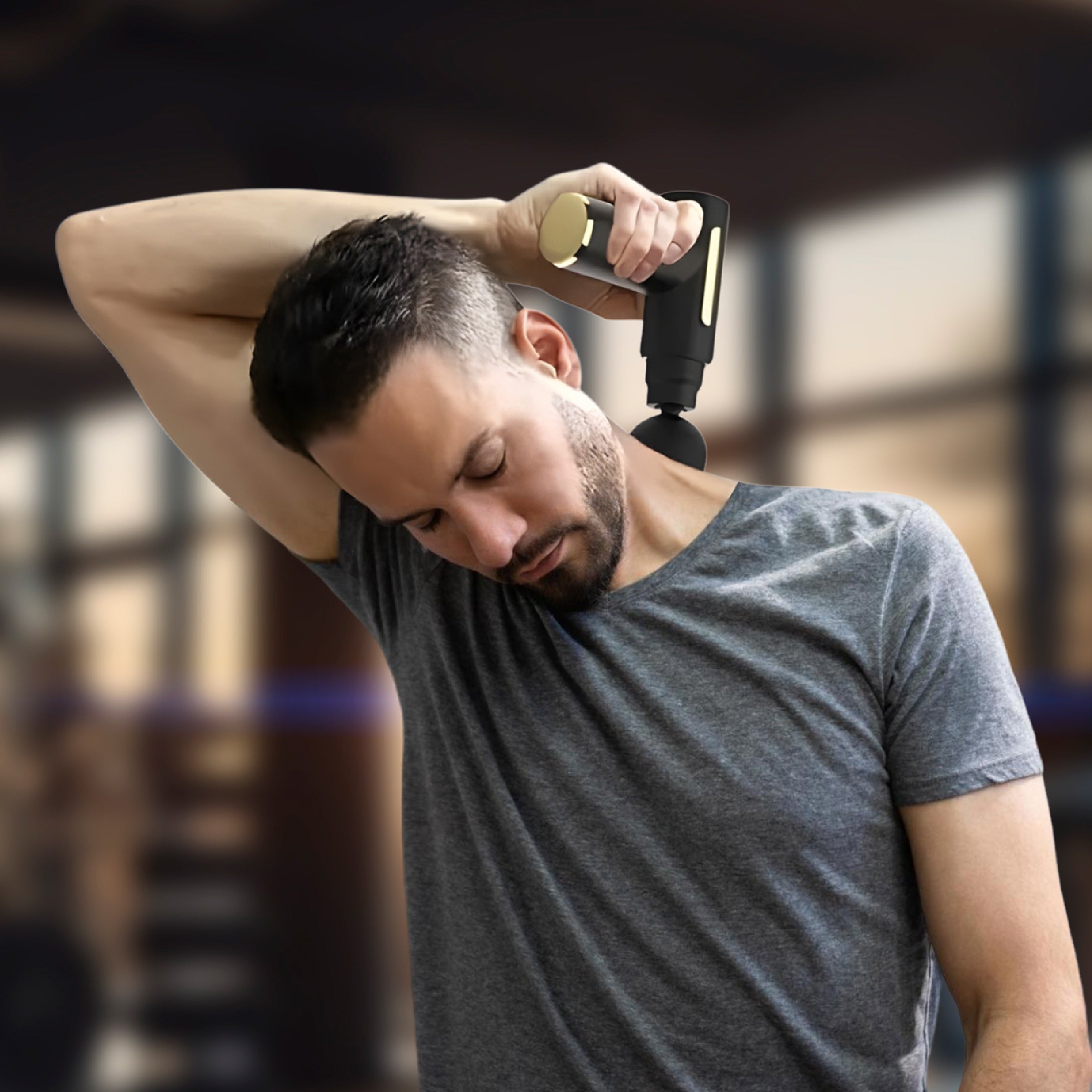 Man using a handheld massager on his arm in a gym setting