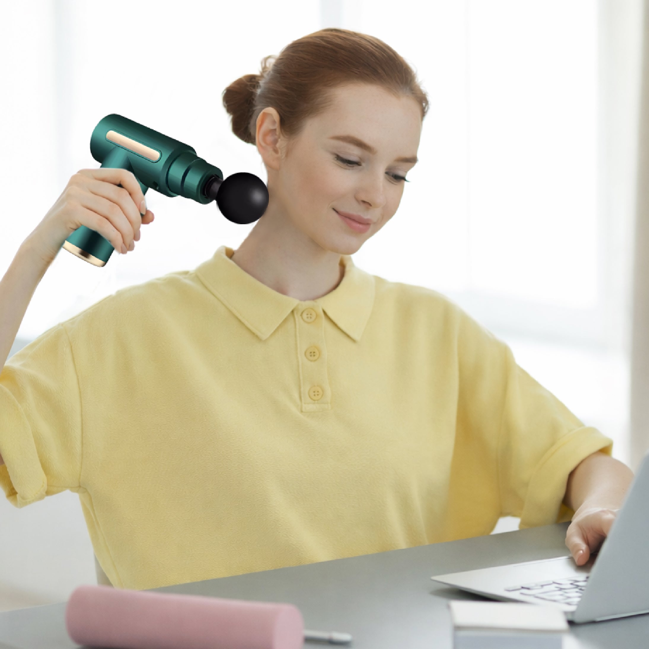 Woman using a green massage gun at a desk with a laptop